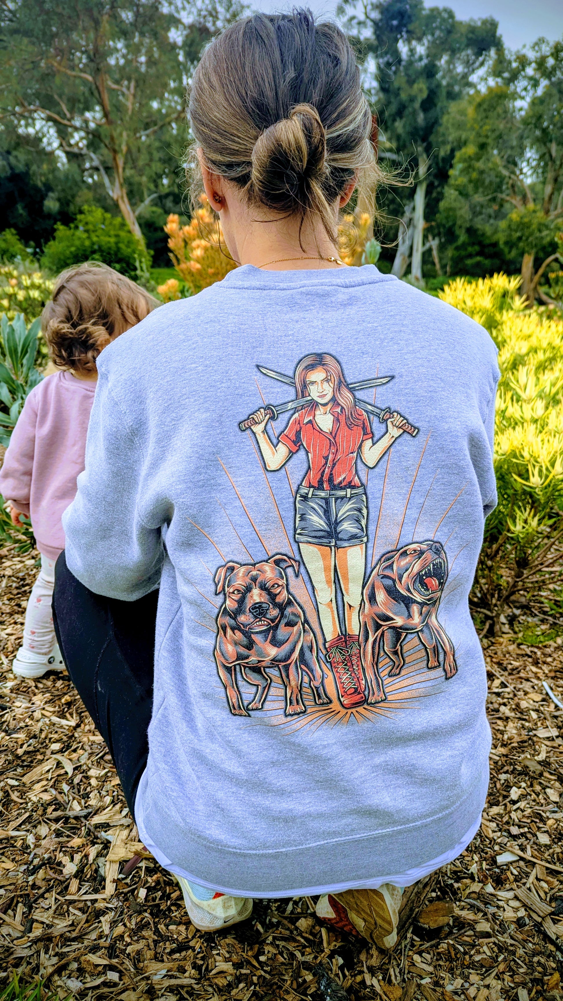 Person wearing a light blue sweatshirt with a graphic design of a woman and two dogs outdoors.