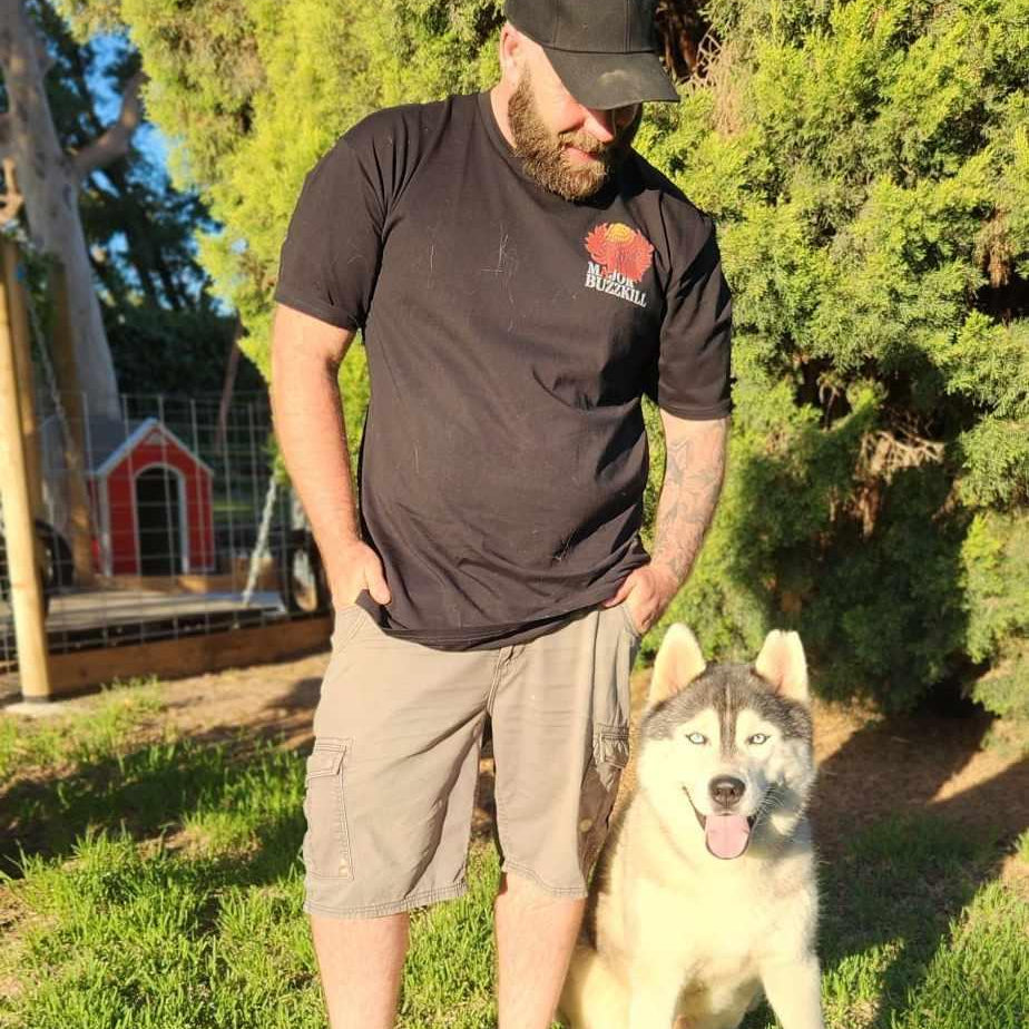 Man with a Major Buzzkill tshirt, standing with a husky, with trees in the background